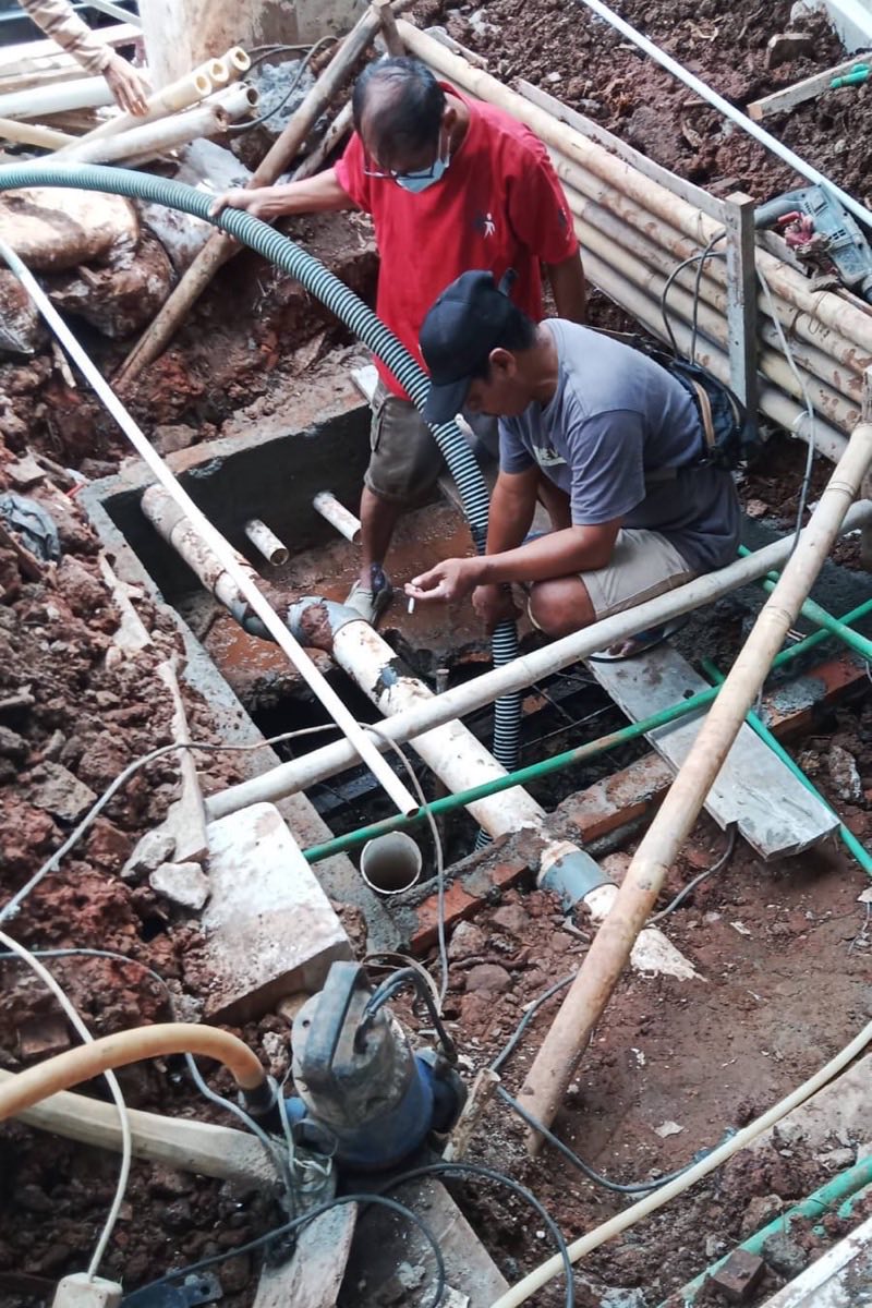 Dua teknisi Kembar Putra mengerjakan jaringan pipa limbah di galian