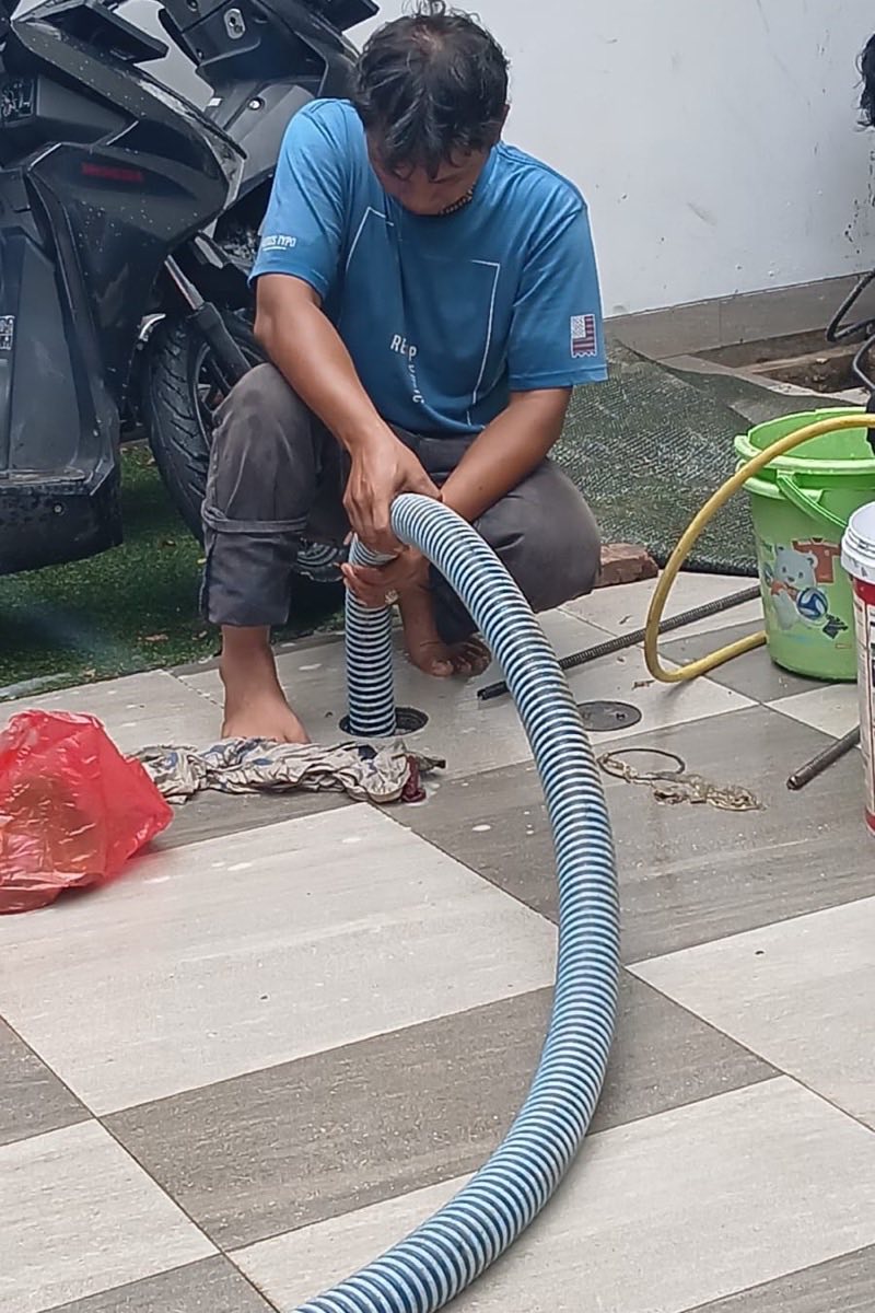 Teknisi memasang selang sedot pada lubang kontrol di halaman rumah