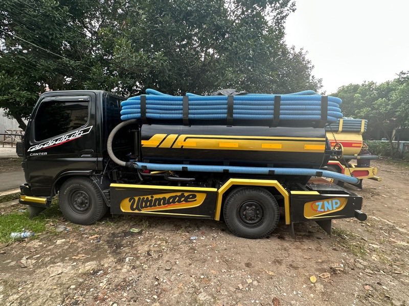 Truk tangki sedot WC Kembar Putra tampak samping dengan gulungan selang